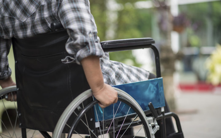 Close Up Of Senior Woman Hand On Wheel Of Wheelchair During Walk